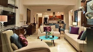 Ein modernes Wohnzimmer mit einer Couch, Sesseln und einem Couchtisch. Im Hintergrund ist eine Küche zu sehen.