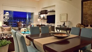 Ein modernes Wohnzimmer mit Essbereich, ausgestattet mit einem großen Fenster, einem Flachbildfernseher und einem Esstisch mit Stühlen.