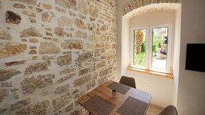 A room with a stone wall, a wooden table with placemats, and a window with a view of greenery. - Galielo Boutique Suite by Corfuescapes  (Corfu)