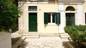 A stone-paved entrance to a building with a green door and shutters, surrounded by greenery. - Galielo Boutique Suite by Corfuescapes  (Corfu)