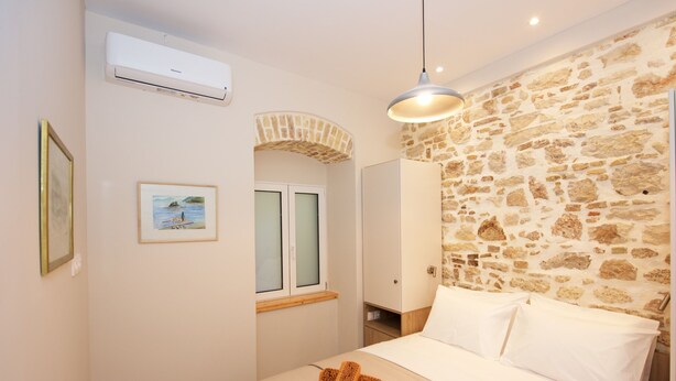 A bedroom with a stone wall, a bed with white linens, a hanging light fixture, and a framed picture on the wall. - Galielo Boutique Suite by Corfuescapes  (Corfu)
