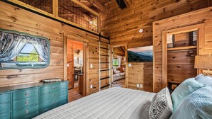 Un dormitorio de cabaña de madera con cama, tocador y vistas al exterior.