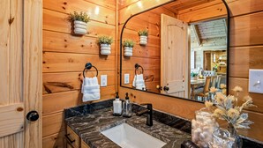 Un baño de estilo cabaña de madera con un lavamanos de mármol, paredes de madera y un espejo grande.