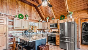 Cocina de cabaña de madera con una isla central, armarios de madera, un refrigerador de acero inoxidable y un ventilador de techo.