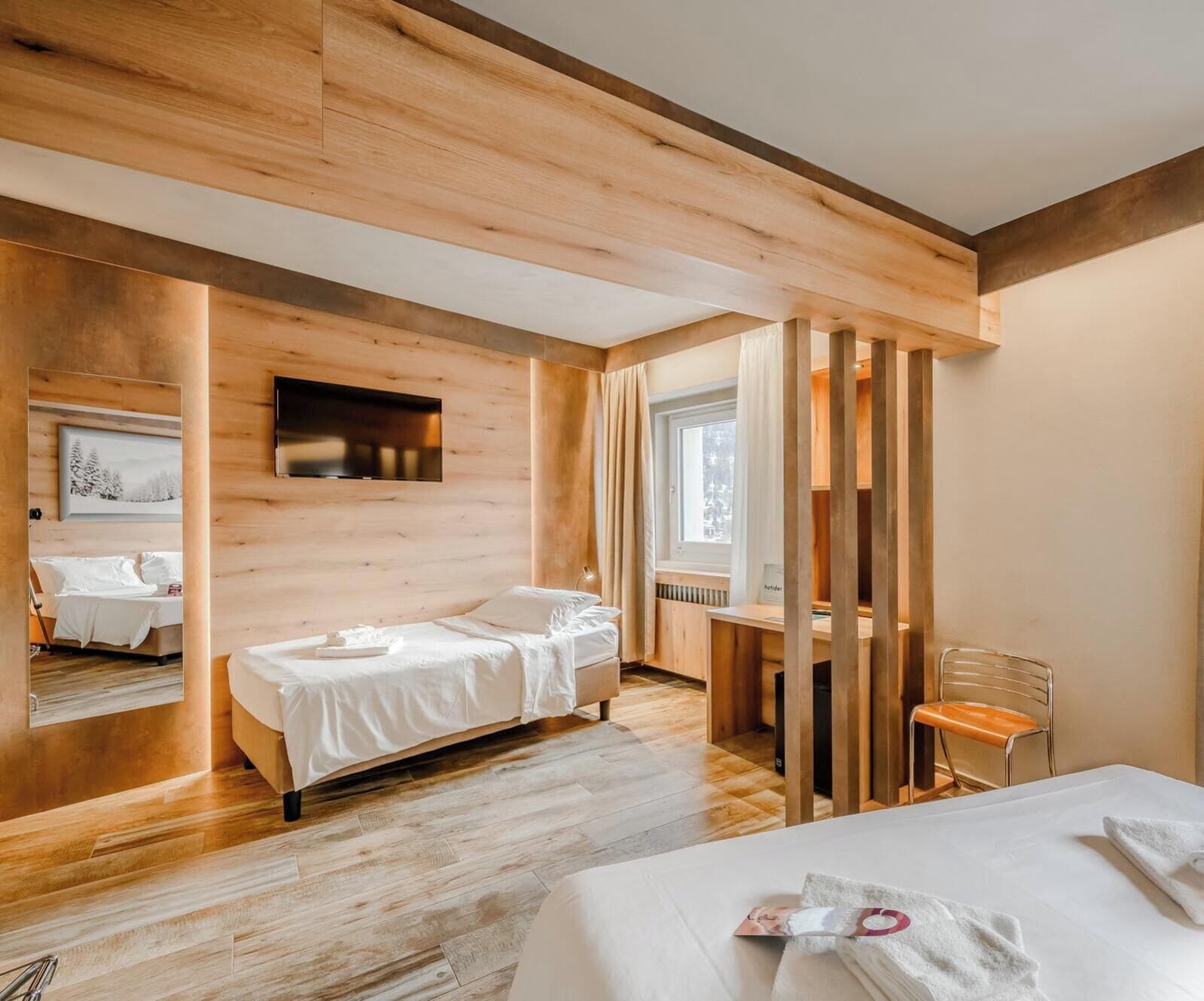 A hotel room with a wooden floor, a bed, a desk, and a chair.