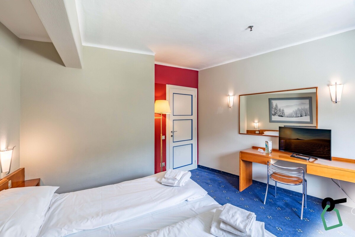 A hotel room with two beds, a desk with a computer, a chair, and a television.