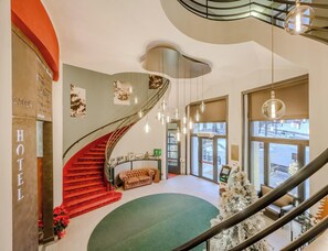 Interior de un hotel con una escalera de caracol, una recepción y un árbol de Navidad.