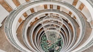 Un atrio de varios niveles con una estructura decorativa central, múltiples pisos con barandillas de vidrio y un piso con diseño.