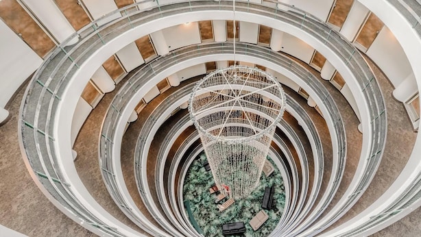 A multi-level atrium with a central decorative structure, multiple floors with glass railings, and a patterned floor. - Hotiday Sauze Torre (Sauze d'Oulx)