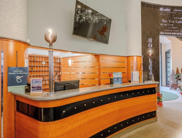 A hotel reception desk with a wooden finish, a mounted television, and a sign for the Holiday Room Collection. - Hotiday Sauze Torre (Sauze d'Oulx)