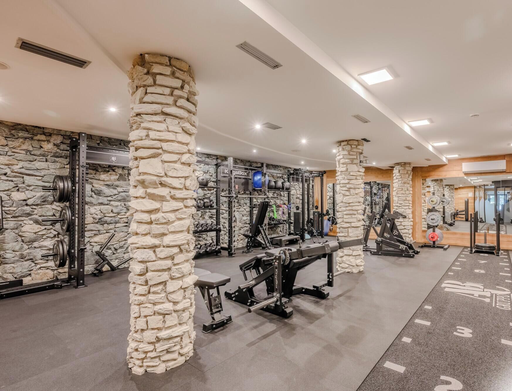 Academia com pilares de pedra, equipamentos de musculação e um espelho grande.