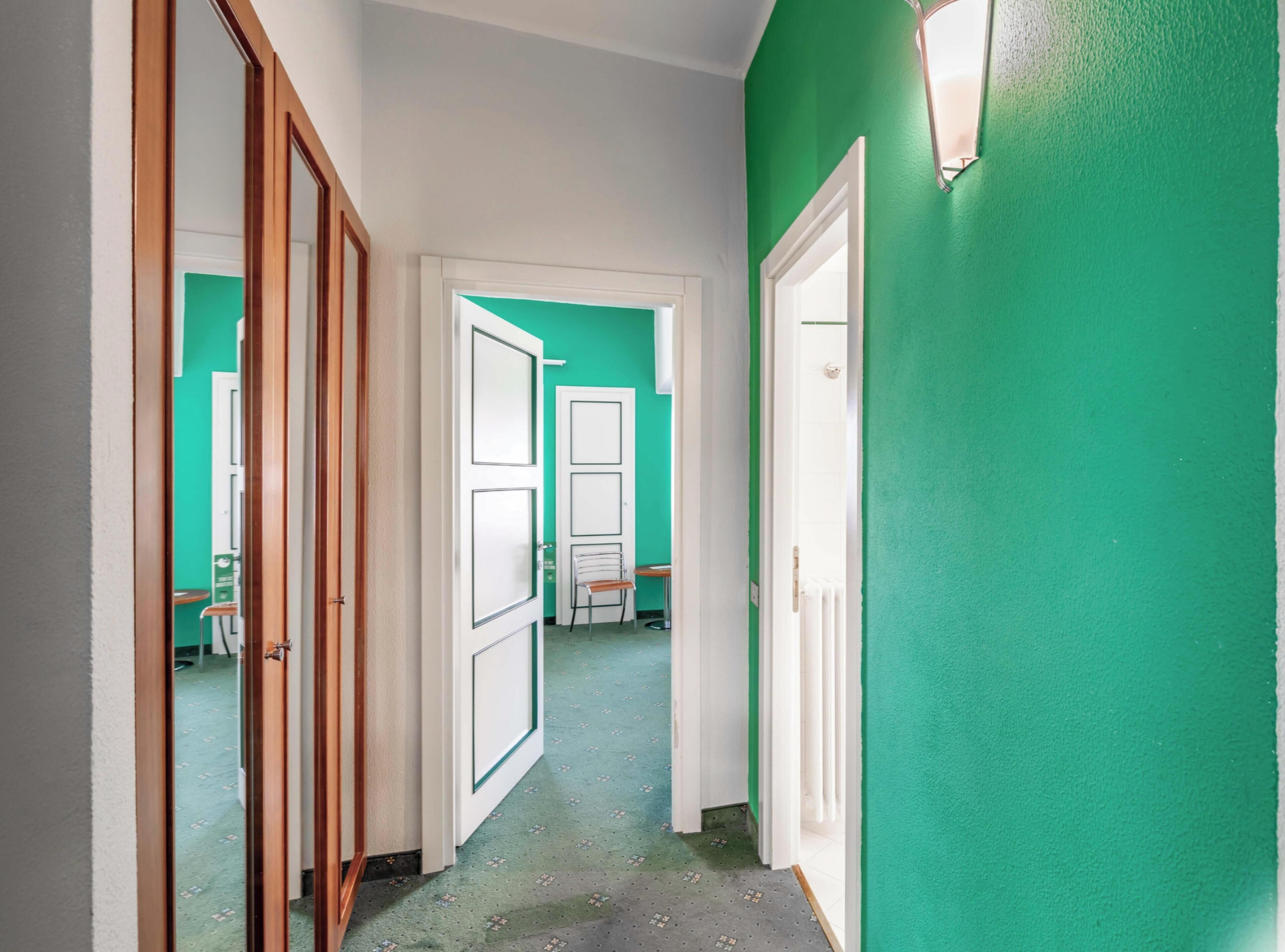 Un couloir avec un mur vert, des portes blanches et un sol à motifs.