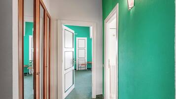 Un couloir avec un mur vert, des portes blanches et un sol à motifs.