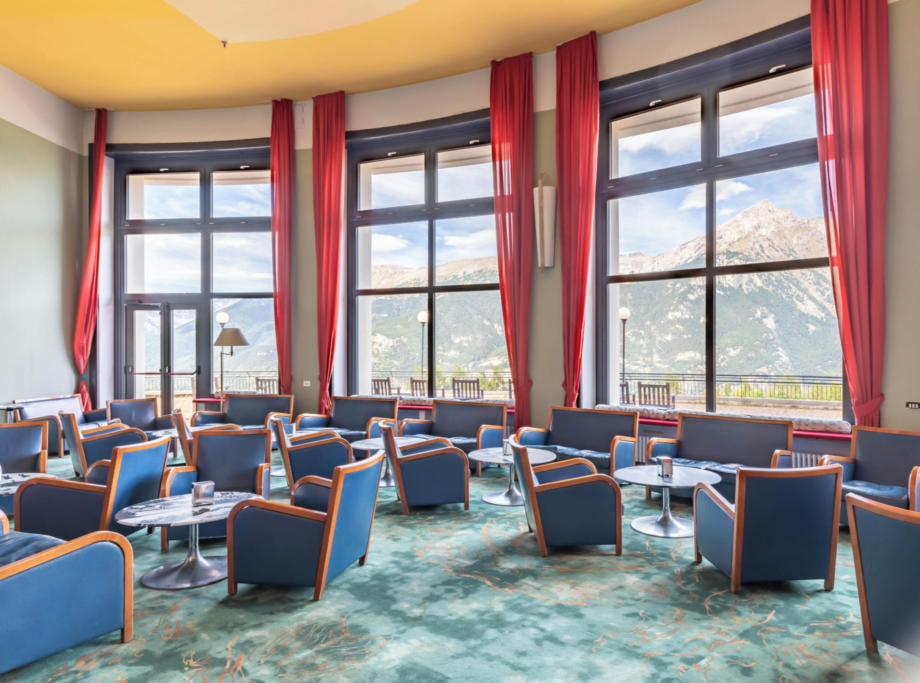 A hotel room with large windows, blue chairs, and a green carpet.