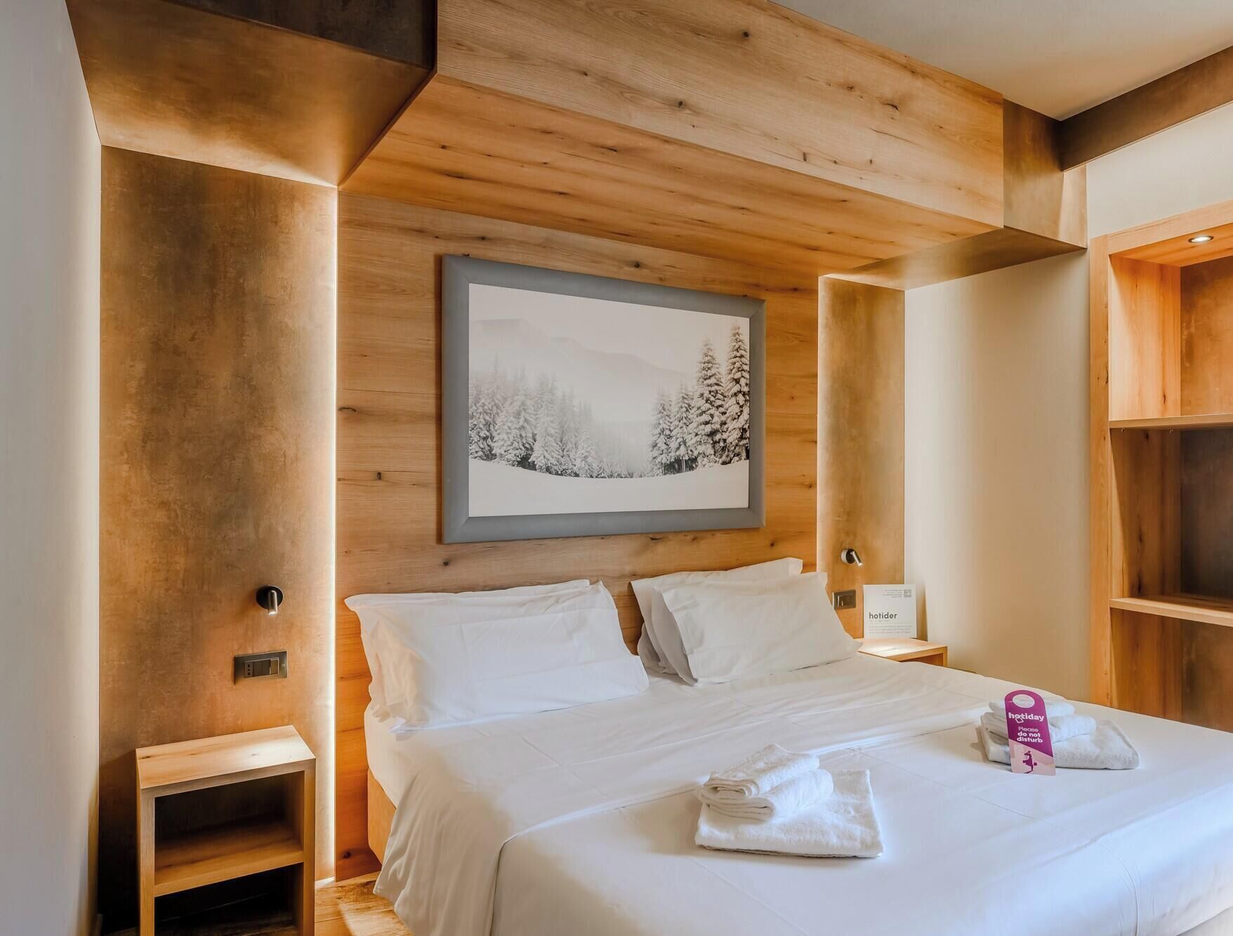 Habitación de hotel con una cama, una mesita de noche, un estante de madera y un cuadro en la pared.