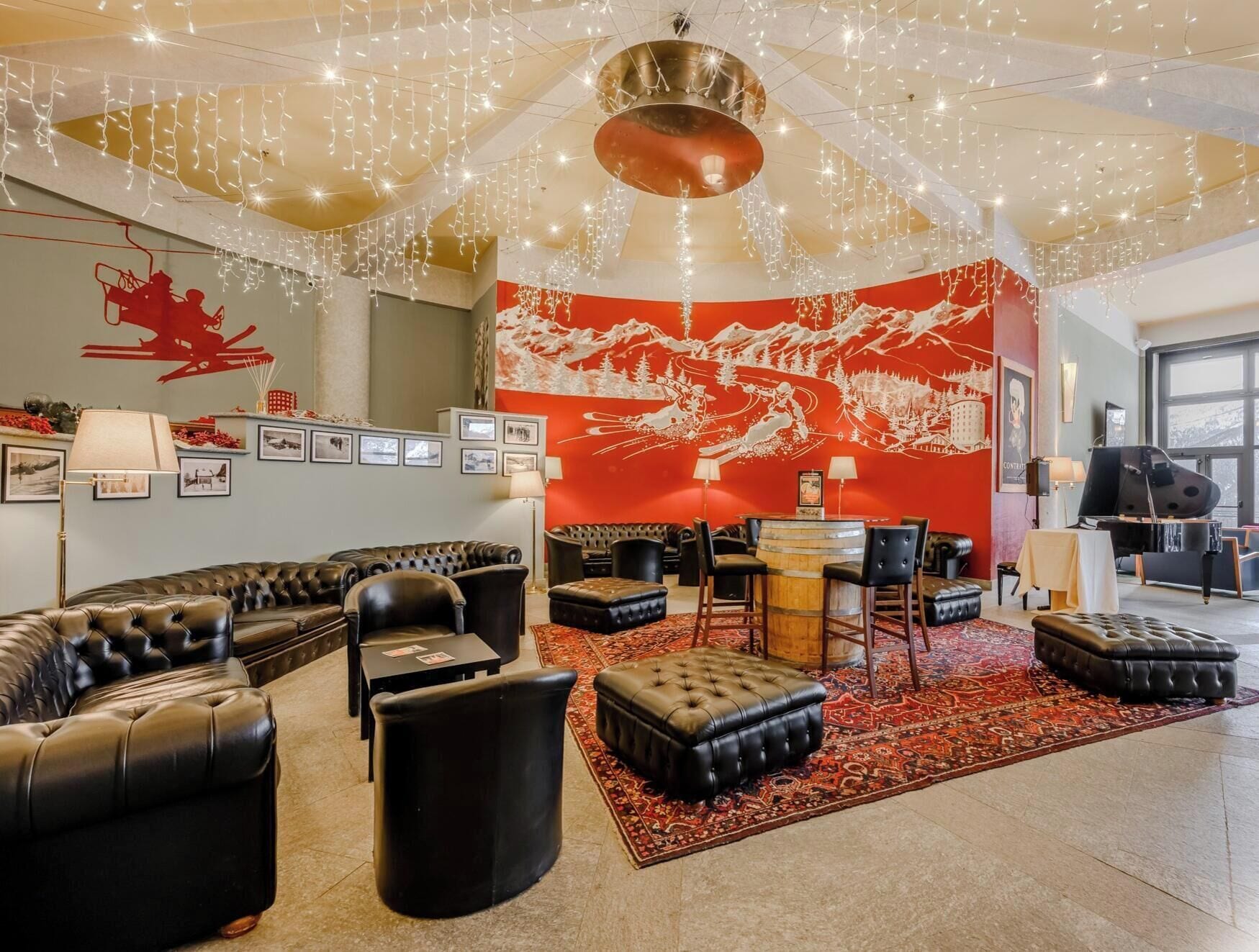 Espaço de descanso com sofás de couro, pufes, tapete vermelho e um mural na parede.