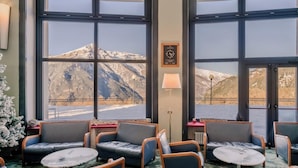 A hotel room with large windows offering mountain views, a cozy seating area with sofas and tables, and a clock on the wall. - Hotiday Sauze Torre (Sauze d'Oulx)