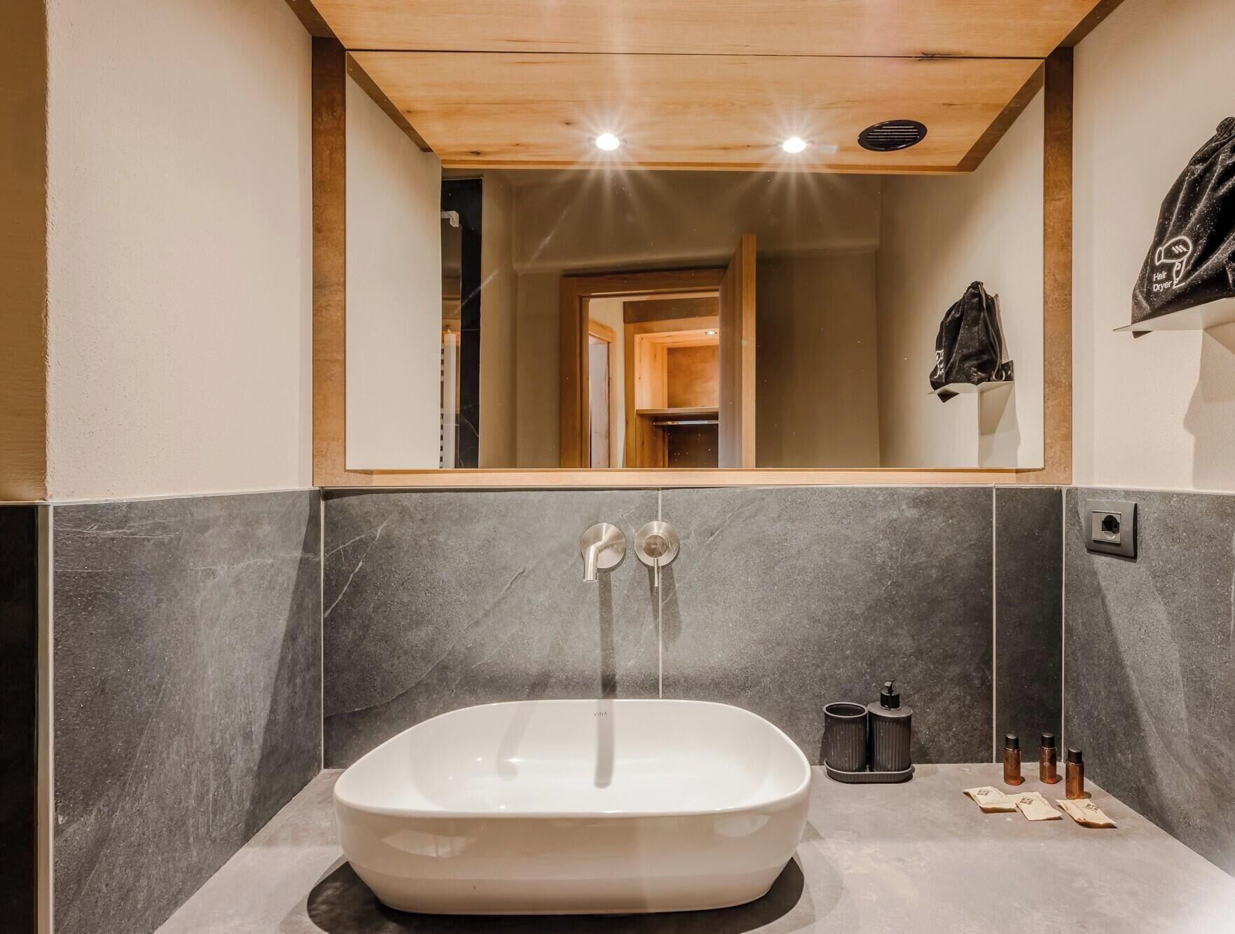 A modern bathroom with a freestanding bathtub, a mirror above the sink, and a wooden ceiling.