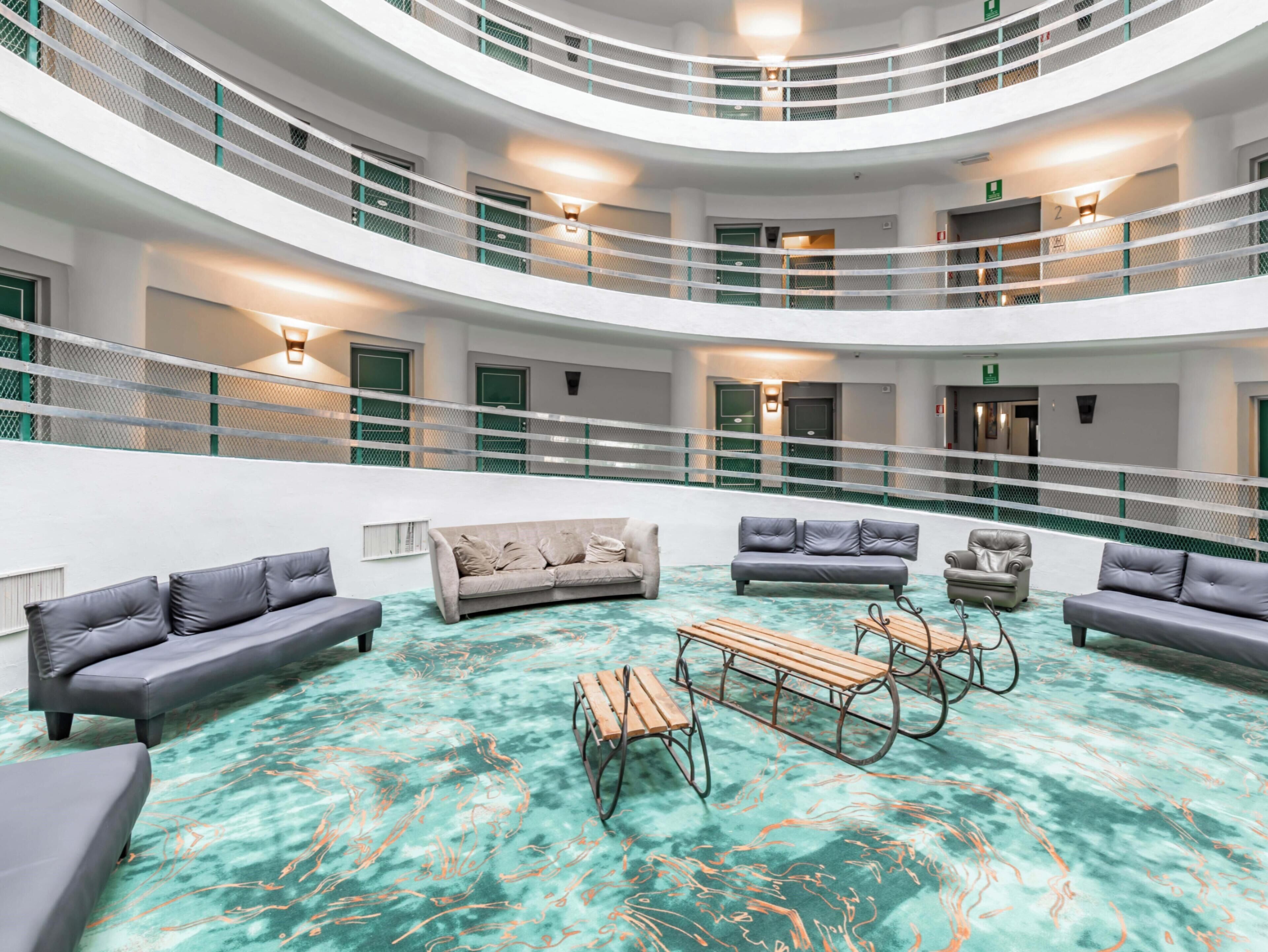 Un hall d’entrée intérieur à plusieurs niveaux, doté d’espaces aménagés avec des sièges et d’une table centrale, et caractérisé par un sol unique en marbre turquoise.