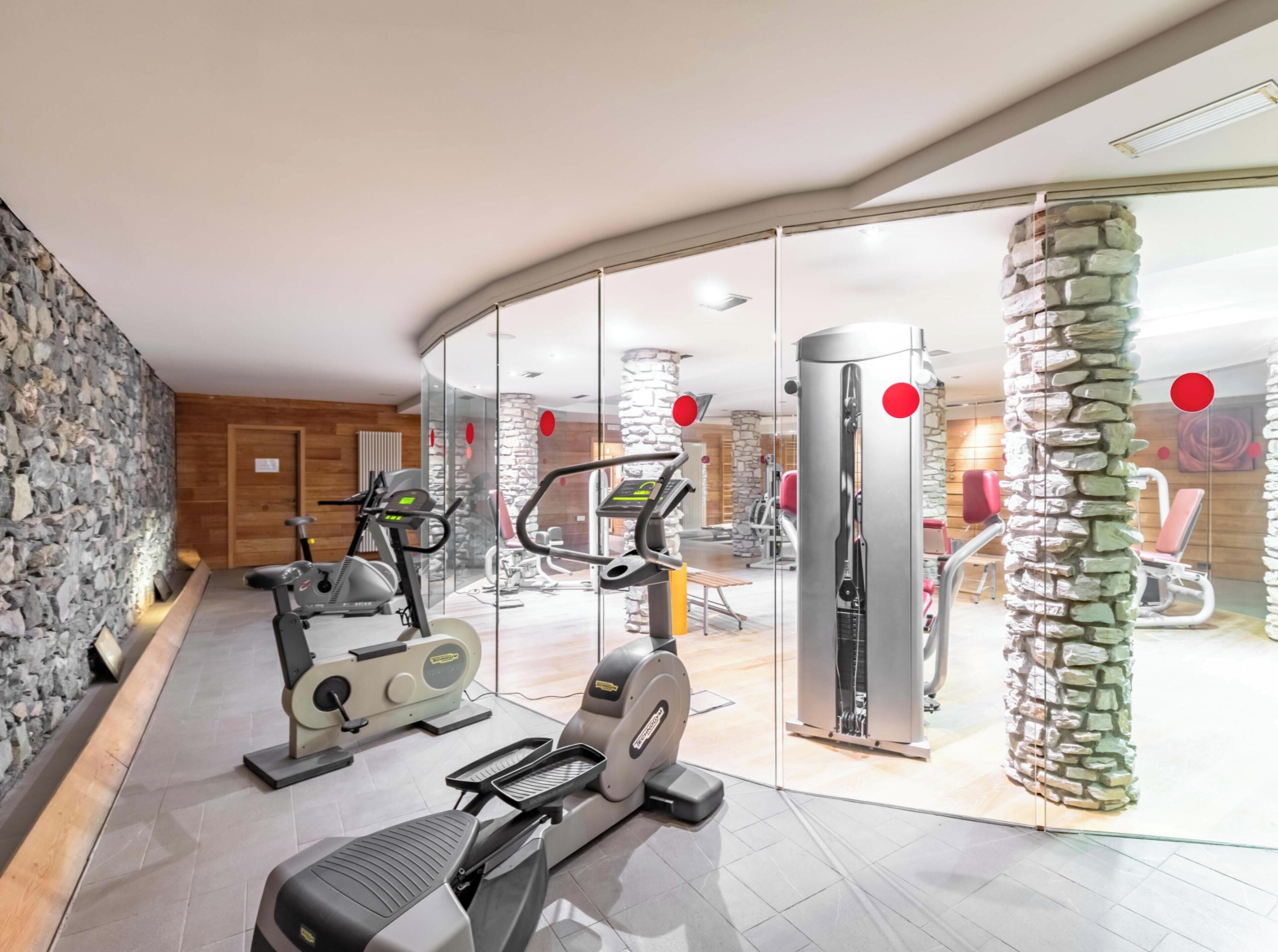 A gym with exercise equipment, stone wall, and a glass partition.