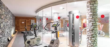 A gym with exercise equipment, stone wall, and a glass partition.