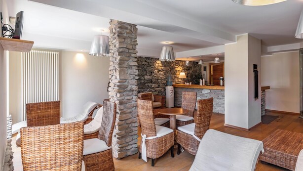 A modern interior with wicker furniture, a stone pillar, and a kitchen area. - Hotiday Sauze Torre (Sauze d'Oulx)