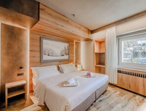 Habitación de hotel moderna con interior de madera, una cama grande, una ventana con vistas a la ciudad y un cuadro en la pared.