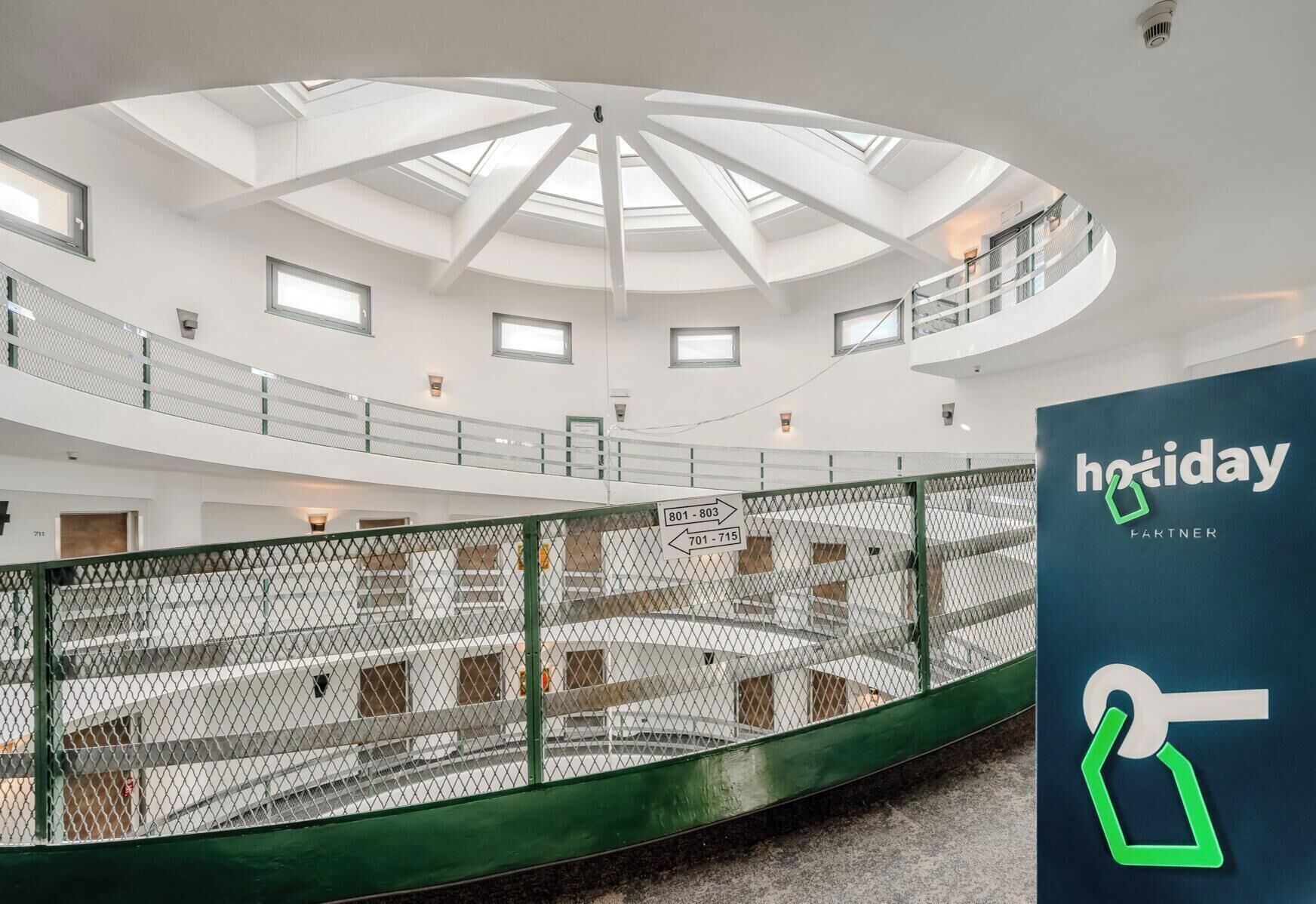 A spacious atrium with a high ceiling and skylights, a green safety railing, and a sign indicating 'hotday partner'.