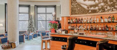 A bar area with a wooden counter, multiple stools, and a Christmas tree.
