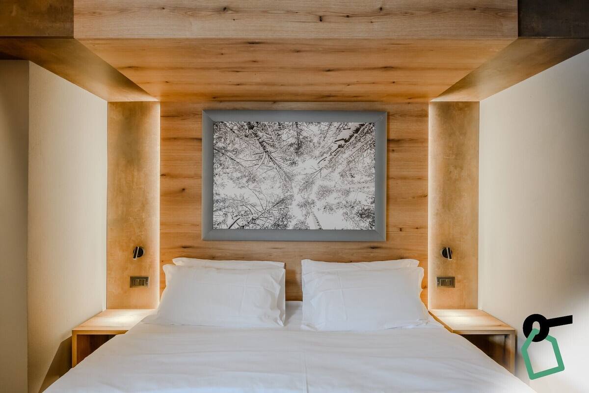 A modern bedroom with a large bed, two bedside tables, and a wall-mounted abstract art piece.