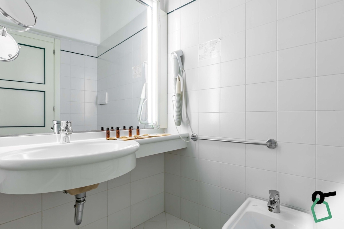 A bathroom with a white sink, a mirror, a towel rack, and a shower area.