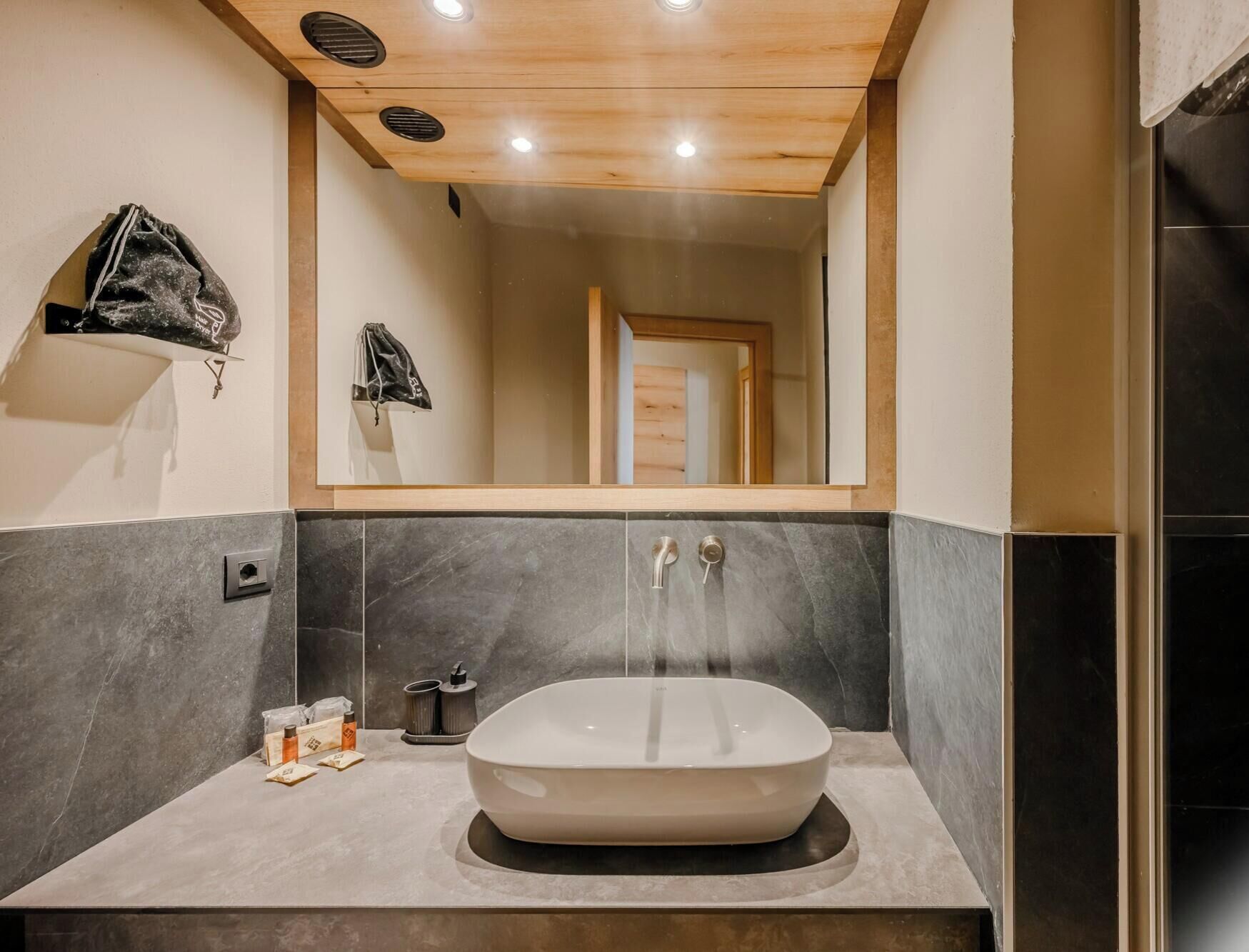 A modern bathroom with a freestanding vessel sink, a mirror above it, and a wooden ceiling.