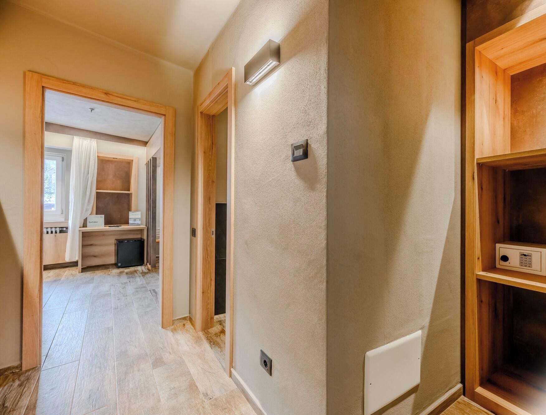 Un pasillo con suelo de madera, un radiador y una puerta que da a una habitación con un escritorio y una silla.