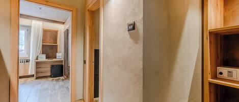 Un pasillo con suelo de madera, un radiador y una puerta que da a una habitación con un escritorio y una silla.