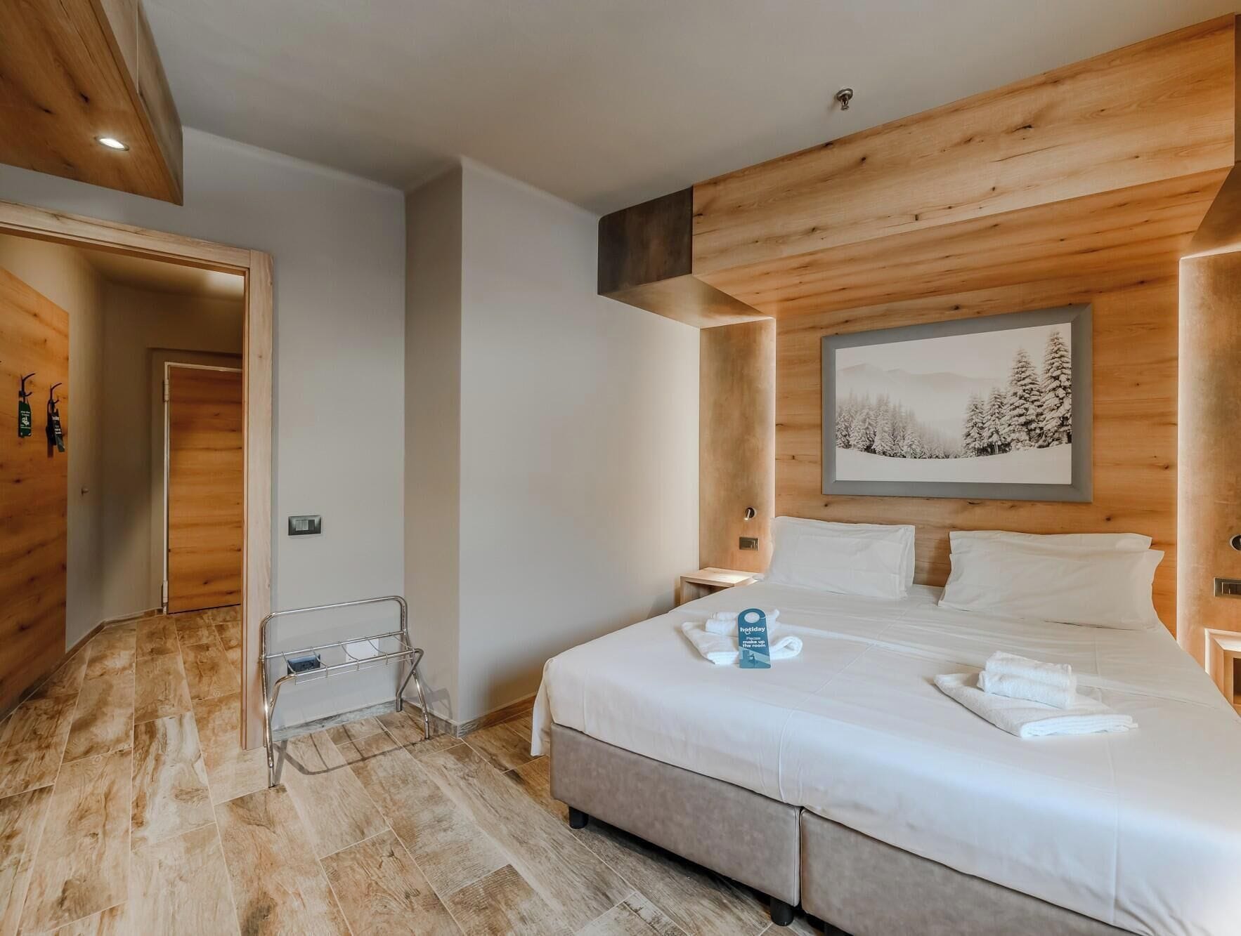 A hotel room with a wooden ceiling, a bed with white linens, a bedside table, and a framed picture on the wall.