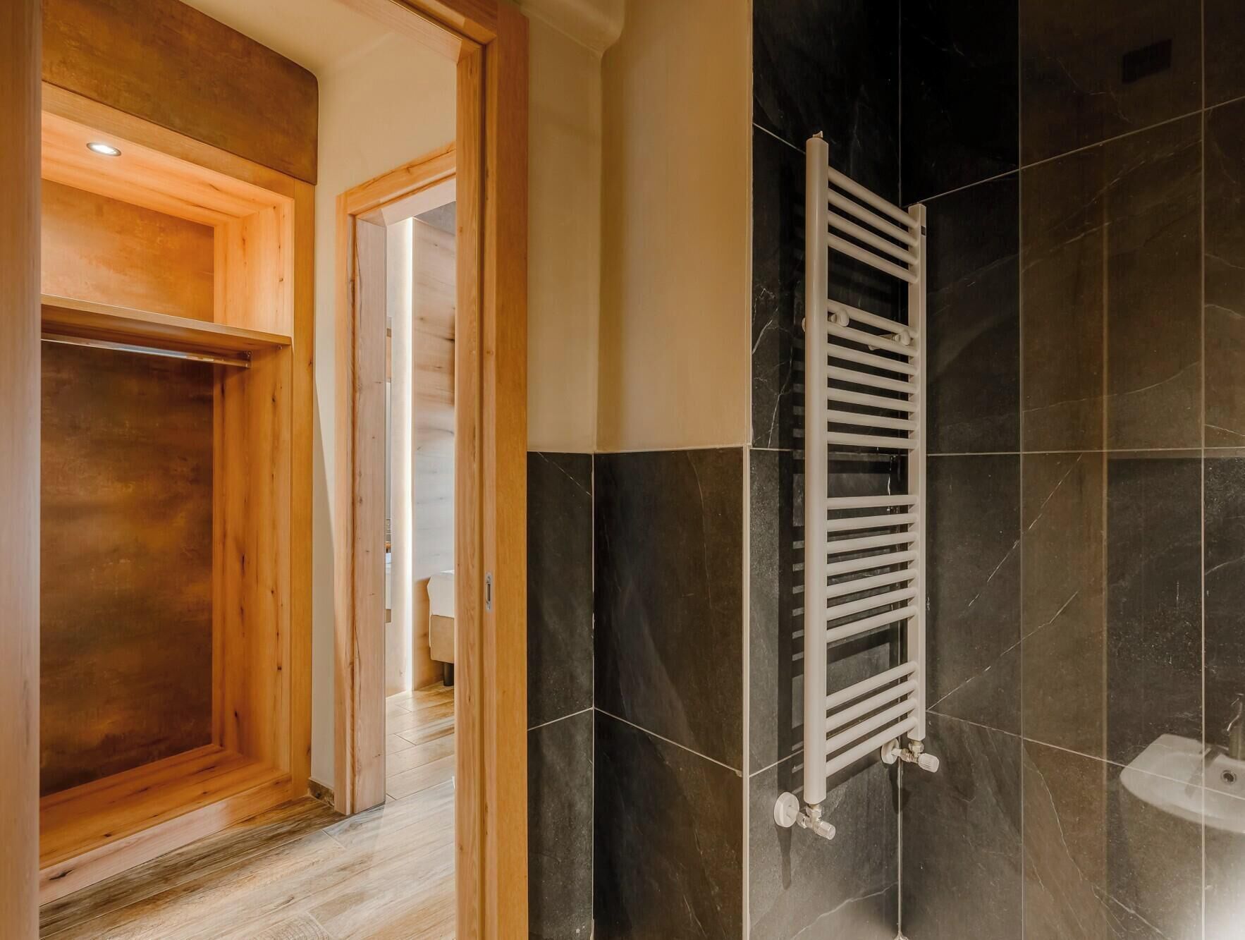 A bathroom with a wooden door, a white towel rack, and dark tiled walls.