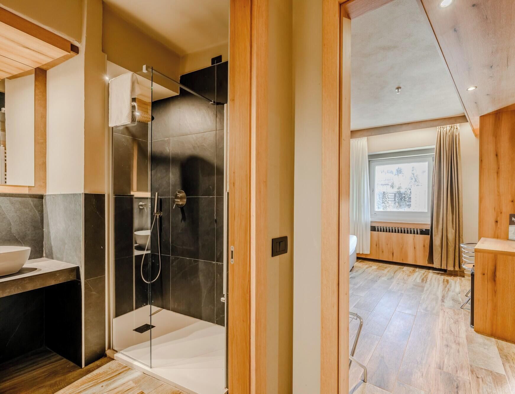 A modern bathroom with a glass-enclosed shower, a wooden vanity, and a large window with a view.
