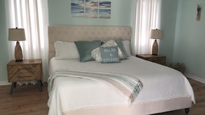 Une chambre à coucher avec un grand lit, deux tables de chevet, une lampe fixée au mur et un tableau.