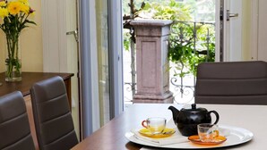 A dining table with a teapot and cups, a vase with yellow flowers, and a view of greenery through a glass door.