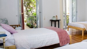 A bedroom with a large bed, a smaller bed, and a nightstand with a book. There is a window with a view of greenery outside.