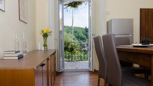 A room with a wooden desk, a chair, a small table with a teapot, and a view of greenery through a glass door.