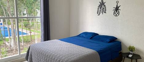 A bedroom with a bed, a small table, and a view of a swimming pool.