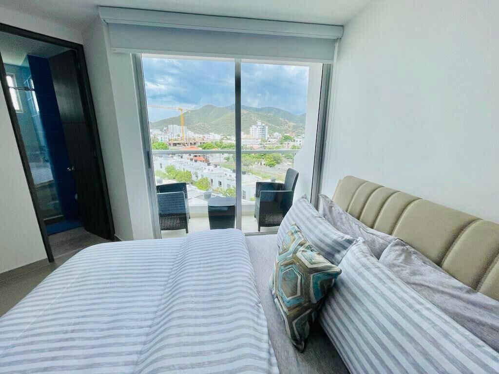 Une chambre à coucher avec un lit, un canapé et une vue sur le paysage urbain, visible à travers de grandes fenêtres.