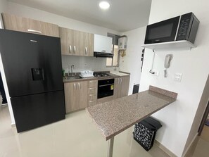 A modern kitchen with a black refrigerator, stainless steel microwave, and a granite countertop. - Modern and exclusive apartment - Rodadero Sur - Santa Marta (Gaira)