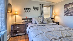 A bedroom with a bed, bedside tables, a desk, a window with blinds, and wall art. - New!Quaint & Convenient Hideaway: Great Location (East Hartford)