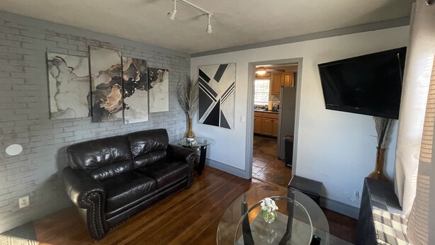A living room with a black leather sofa, a glass coffee table, and abstract wall art. - New!Quaint & Convenient Hideaway: Great Location (East Hartford)