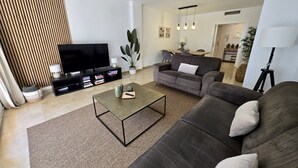 Un soggiorno moderno con una TV a schermo piatto, un divano, un tavolino e, sullo sfondo, una zona pranzo.