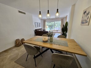 A dining area with a wooden table, two chairs, a vase with flowers, and hanging light fixtures.
