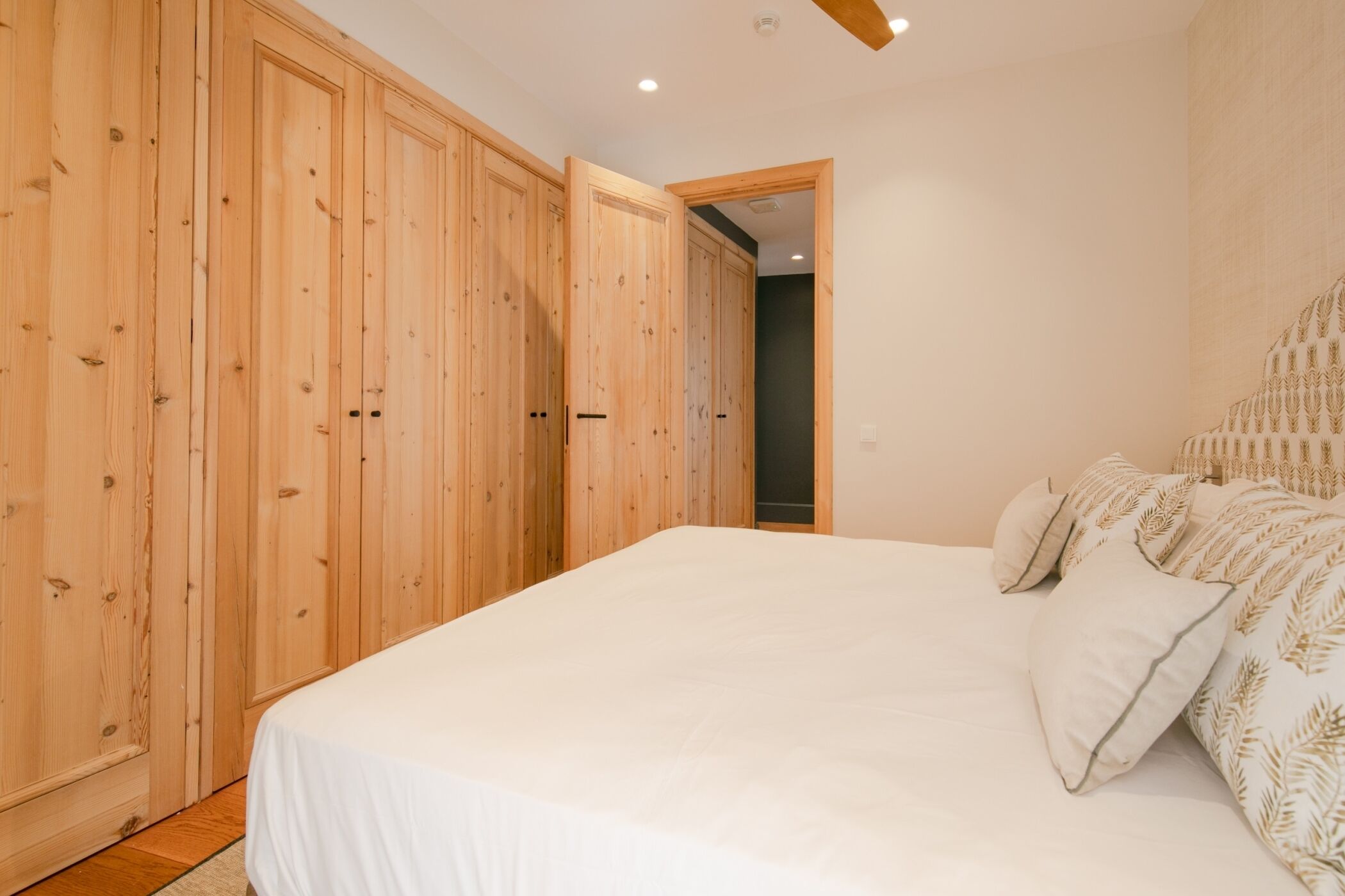 A bedroom with a large bed, wooden wardrobe, and a door leading to another room.