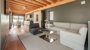 Un salon moderne avec un plafond en bois, un canapé blanc, une table basse en verre et un coin repas comprenant des chaises et une table en bois.